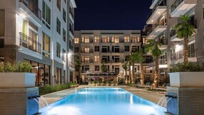 A modern hotel with a central swimming pool, multiple balconies, and outdoor seating areas. - New! Master Suite w/ Skyline Views - Art Dist (Houston)