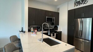 A modern kitchen with a central island, stainless steel appliances, and a 'Home Sweet Home' sign. - New! Master Suite w/ Skyline Views - Art Dist (Houston)