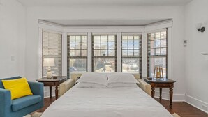Une chambre à coucher avec un grand lit, un fauteuil bleu et une vue sur l’extérieur grâce à une grande baie vitrée.