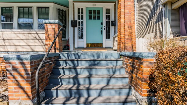 Une maison à deux étages avec une porte d’entrée bleu clair, une façade en briques et un escalier menant au porche avant.