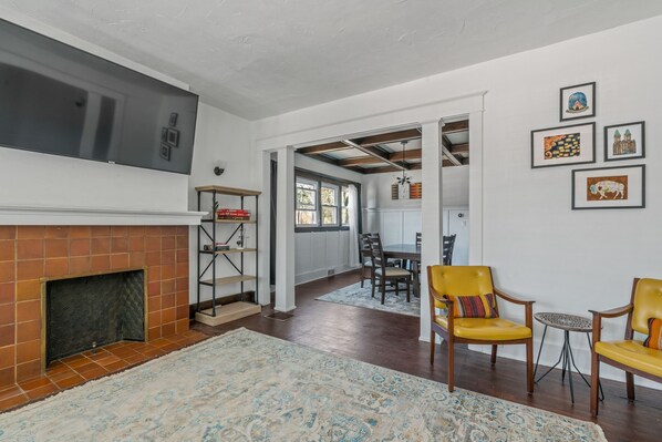 A spacious living room with a fireplace, yellow chairs, a dining area, and artwork on the walls.