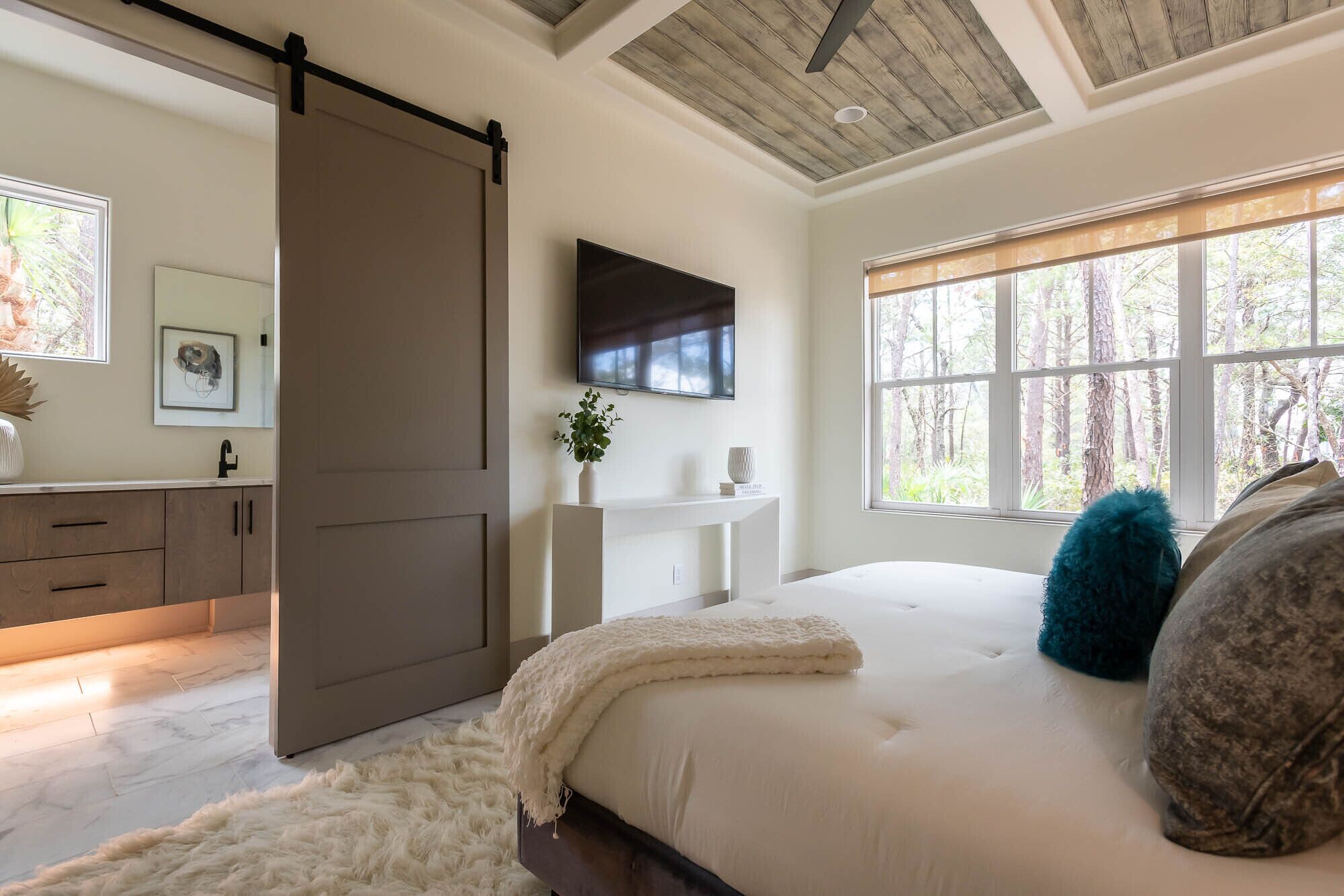 A bedroom with a large bed, a sliding door closet, a mounted TV, and a window with a forest view.