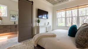 Une chambre dotée d’un grand lit, d’un placard avec porte coulissante, d’un téléviseur fixé au mur et d’une fenêtre donnant sur la forêt.