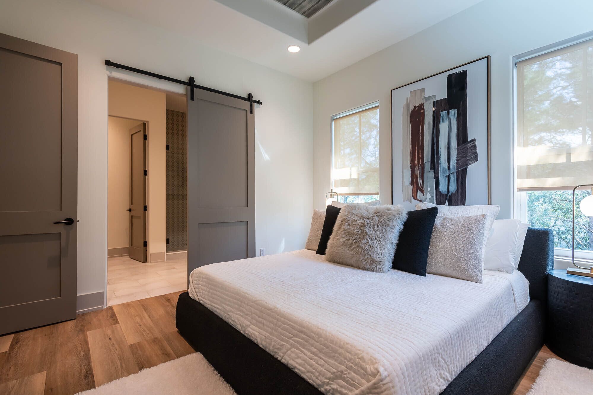 A bedroom with a bed, a sliding door, a window, and a painting on the wall.
