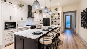 Une cuisine moderne avec des meubles blancs, un îlot central doté de tabourets de bar, un réfrigérateur noir et des luminaires suspendus.
