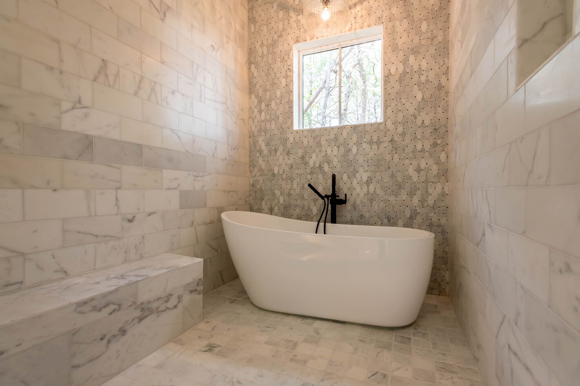 A bathroom with a freestanding bathtub, a window, and marble walls.