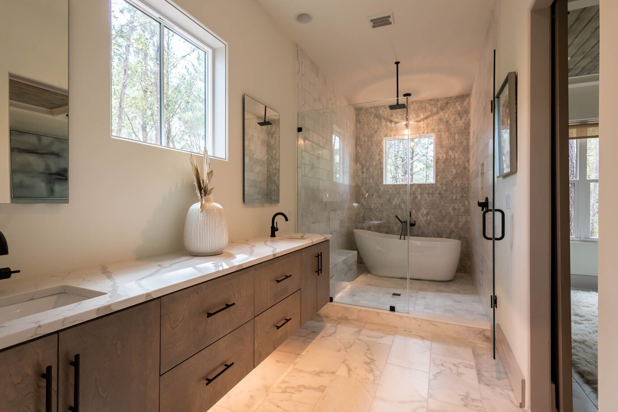 A modern bathroom with a freestanding bathtub, a large mirror, and a window providing natural light.