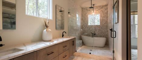 A modern bathroom with a freestanding bathtub, a large mirror, and a window providing natural light.