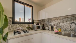 Eine moderne Küche mit weißen Schränken, einer Marmor-Spritzschutzleiste, einem Fenster mit Blick auf die Stadt und einem Spülbecken.