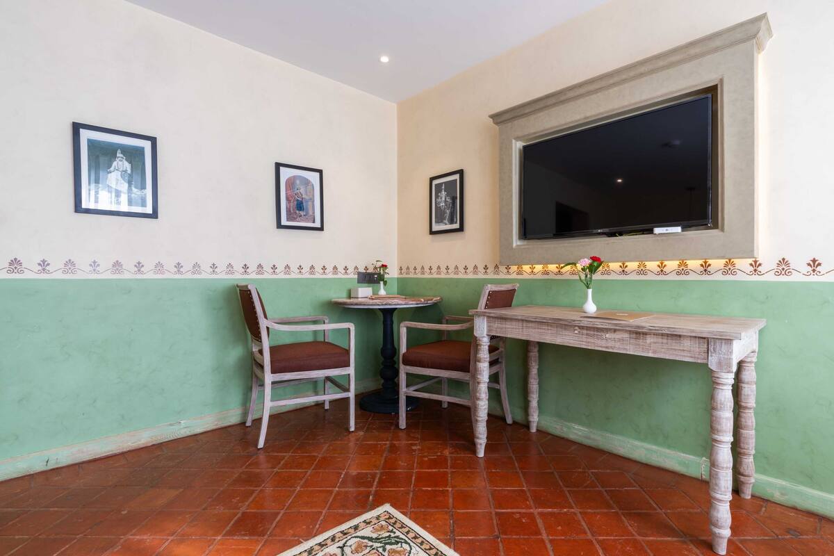 Une pièce d’angle avec deux chaises, une petite table ronde et un téléviseur fixé au mur.