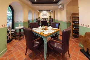 A dining area with a wooden table set for four, surrounded by leather chairs. - Seto Ghar Hotel Pvt. Ltd. (Kathmandu)