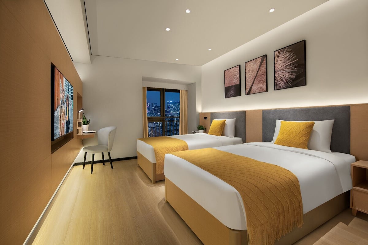 A modern hotel room with two beds, a desk, and a chair.