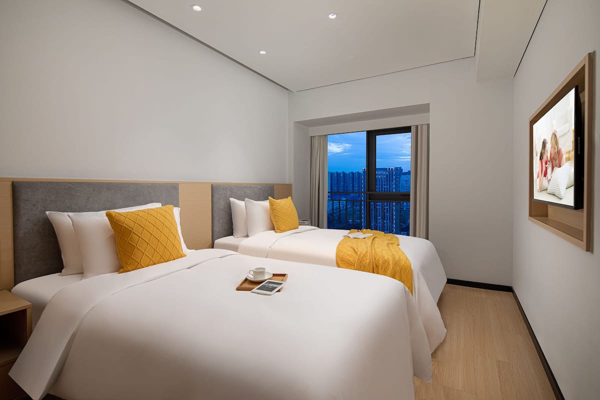 A hotel room with two beds, a large window with a city view, and a framed picture on the wall.