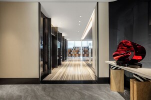 Corredor moderno de hotel, com piso de madeira, paredes estampadas em preto e branco e uma escultura vermelha em pedestal.