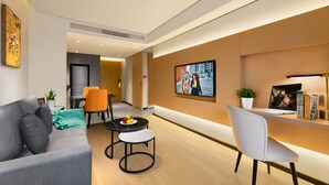 A modern living room with a sofa, two chairs, a small table with fruit, a TV, and a laptop on a desk. - Citadines Gaoxin Chengdu (Chengdu)