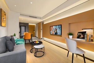 Una sala de estar moderna con un sofá, dos sillones, una mesita baja con fruta, un televisor y una computadora portátil sobre un escritorio.