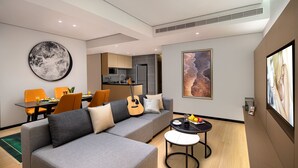 A modern living room with a grey sofa, orange chairs, a dining area with a table, and a kitchen in the background. - Citadines Gaoxin Chengdu (Chengdu)