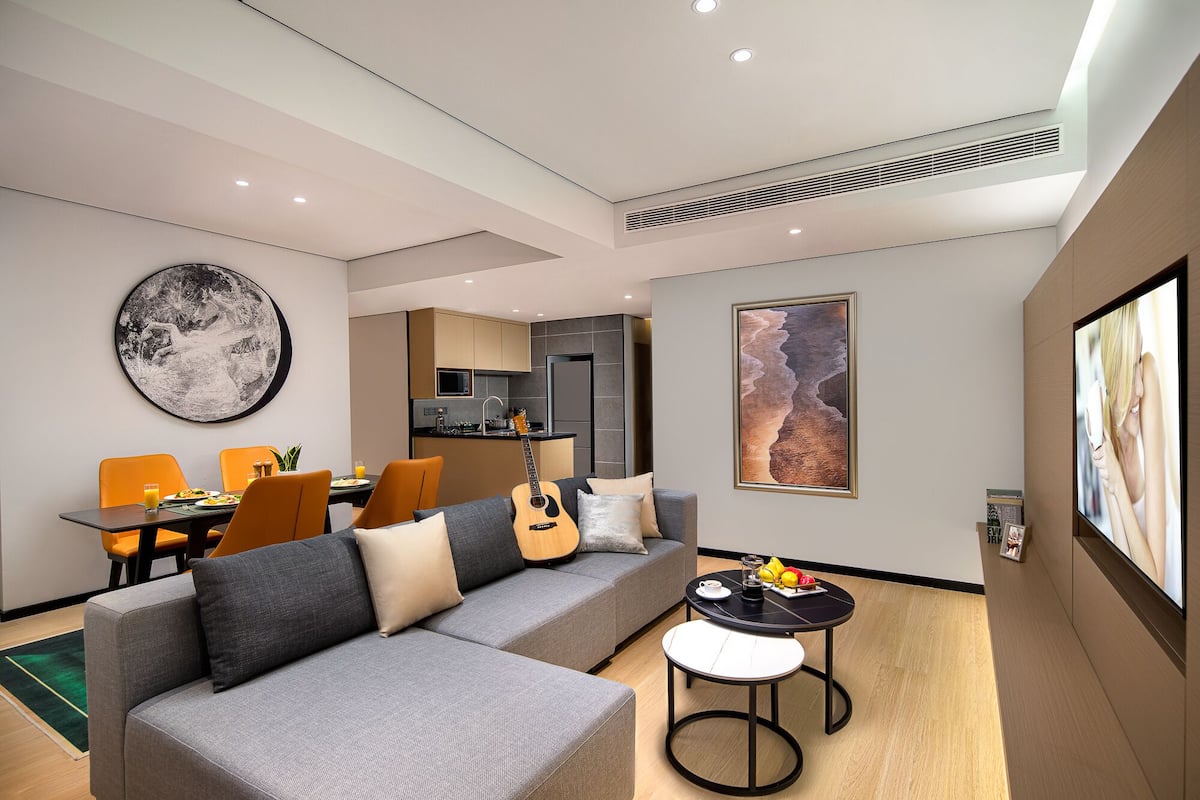 A modern living room with a grey sofa, orange chairs, a dining area with a table, and a kitchen in the background.
