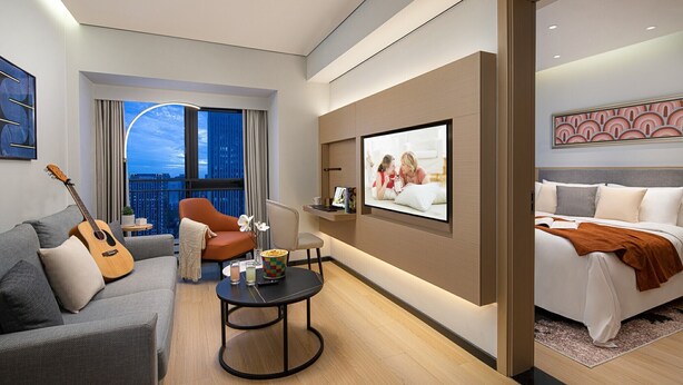 A modern hotel room with a balcony, a bed, a sofa, a coffee table, and a TV mounted on the wall. - Citadines Gaoxin Chengdu (Chengdu)