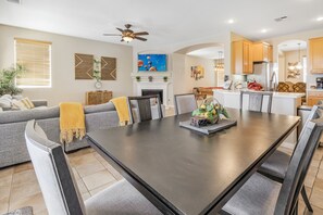 A modern living room with a dark wooden dining table, grey sofas, and a fireplace.