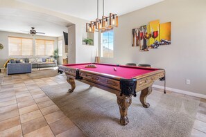 A pool table in a living room with a sofa and a ceiling fan.