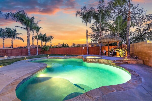 A swimming pool with a curved design, surrounded by a wooden fence and palm trees.
