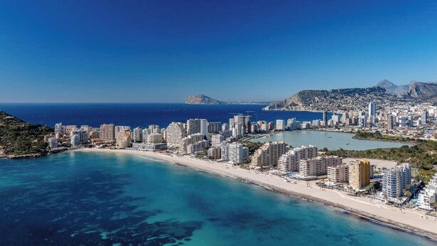 Un paysage urbain côtier avec de hauts immeubles, une plage et une chaîne de montagnes en arrière-plan.