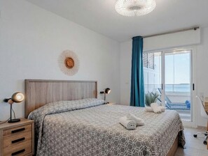 Un dormitorio con cama, lámparas de noche, mesita de noche, un adorno en la pared y vistas al exterior.