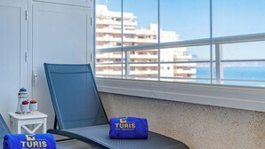 Un balcon avec une chaise, une petite table agrémentée d’objets décoratifs, et une vue sur les bâtiments et la mer.