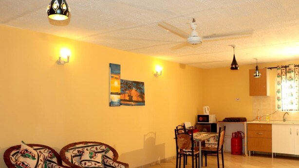 A compact living space with a dining area, kitchen, and two wicker chairs with patterned cushions. - Stay.Plus Kikambala Holiday Home (Mtwapa)