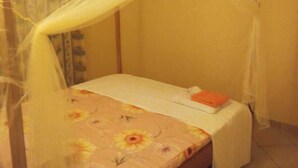 A single bed with a canopy, a floral bedspread, and a small bedside table with an orange object. - Stay.Plus Kikambala Holiday Home (Mtwapa)