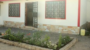 A building with a tiled entrance, two windows with decorative grills, and a small garden area with plants and flowers. - Stay.Plus Kikambala Holiday Home (Mtwapa)