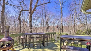 Eine Holzterrasse mit Grill und Feuerstelle, umgeben von Bäumen.