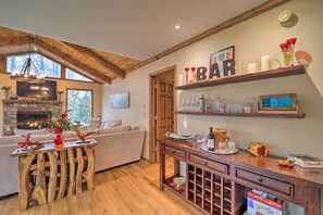 A cozy living room with a fireplace, a wooden coffee table, a sofa, and a bar area with shelves and wine glasses. - Pool & Lake Access: Mtn-View Cottage in Newland (Newland)