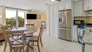 A modern kitchen with white cabinets, a stainless steel refrigerator, a microwave, and a stove. There is a dining area with a round table and wooden chairs. - IN-UNIT WASHER/DRYER | WALK-IN CLOSET | FREE WIFI | KING BED + QUEEN SLEEPER | STEPS TO BONITA BEACH (Bonita Springs)