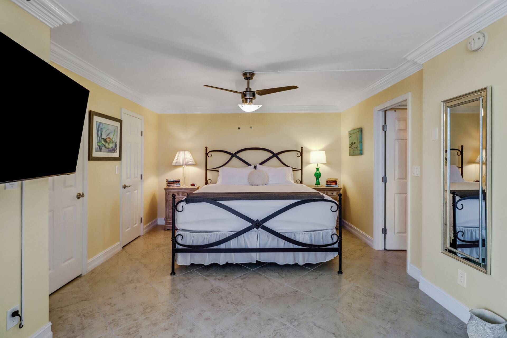 A bedroom with a bed, two bedside tables, a ceiling fan, and a large mirror.