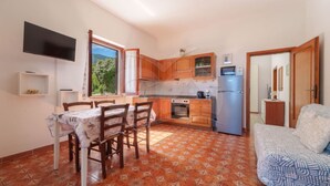 Una cocina compacta con armarios de madera, un horno integrado y un refrigerador. Hay una mesa de comedor con sillas y un sofá en la sala.