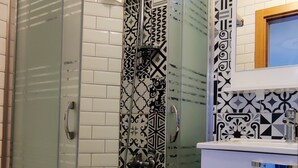 A bathroom with a glass-enclosed shower, white tiled walls, and a patterned floor. - Arslan Homes3 (Muğla)