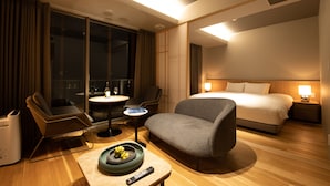 Ein Hotelzimmer mit einem Bett, einer Sitzecke mit Tisch, einem Sessel und einem kleinen Tisch mit Fernbedienung.