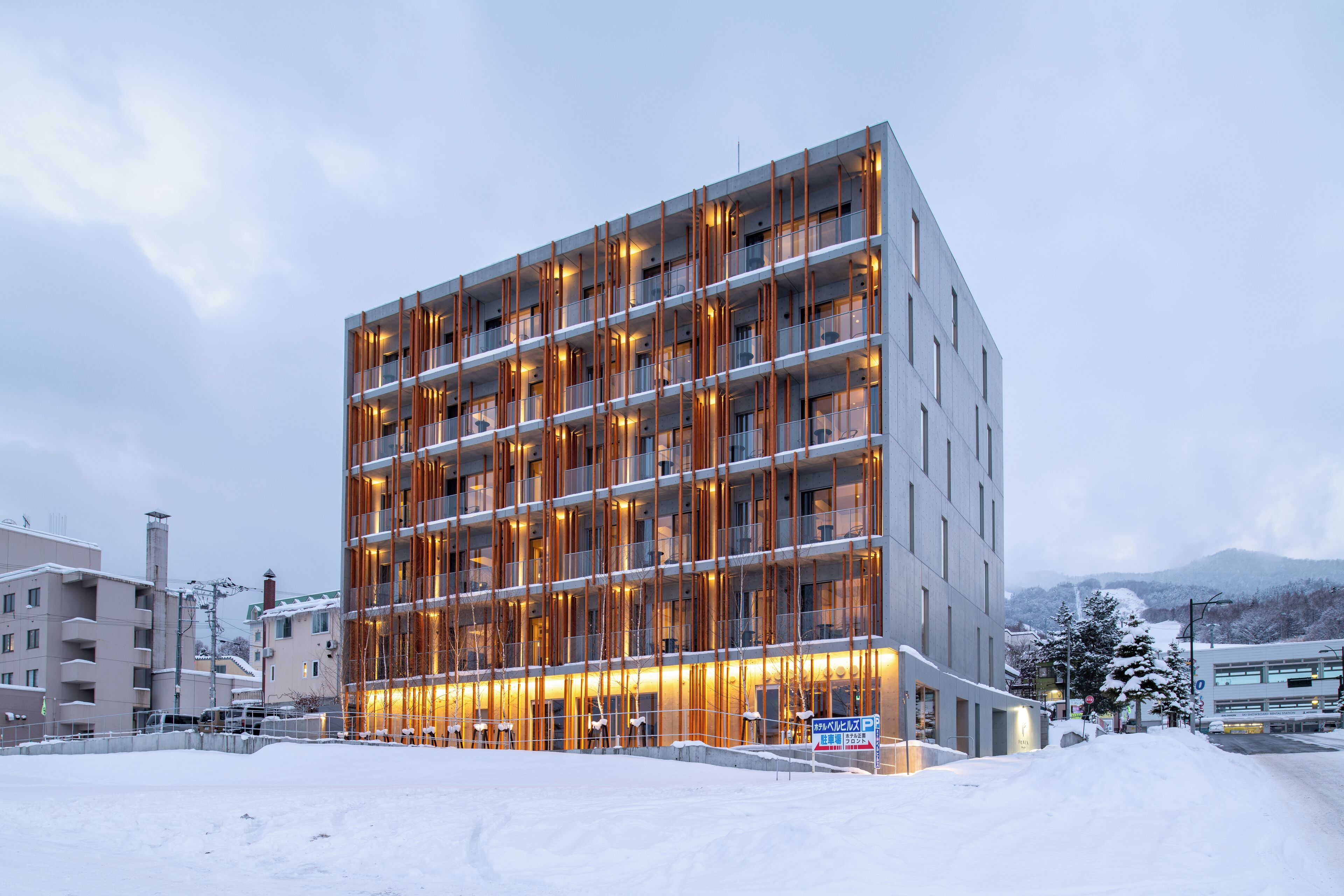 Un hotel moderno de varios pisos con una fachada destacada, grandes ventanales y el suelo cubierto de nieve.