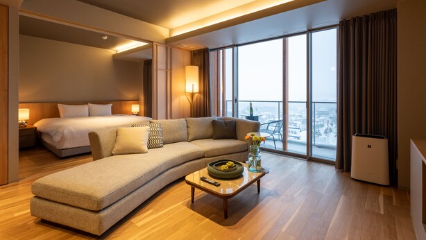Ein modernes Hotelzimmer mit einem großen Bett, einer Couch, einem Couchtisch mit Blumen und Blick auf die Stadt.