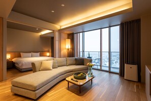 Une chambre d’hôtel moderne avec un grand lit, un canapé, une table basse agrémentée de fleurs et une vue sur la ville.