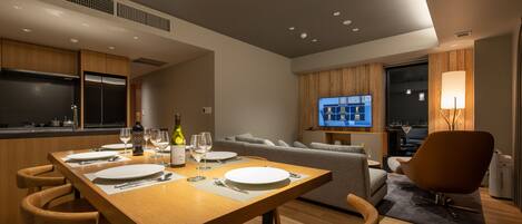 Una sala de estar moderna con una mesa de comedor de madera preparada para cuatro personas, un sofá y un televisor montado en la pared.