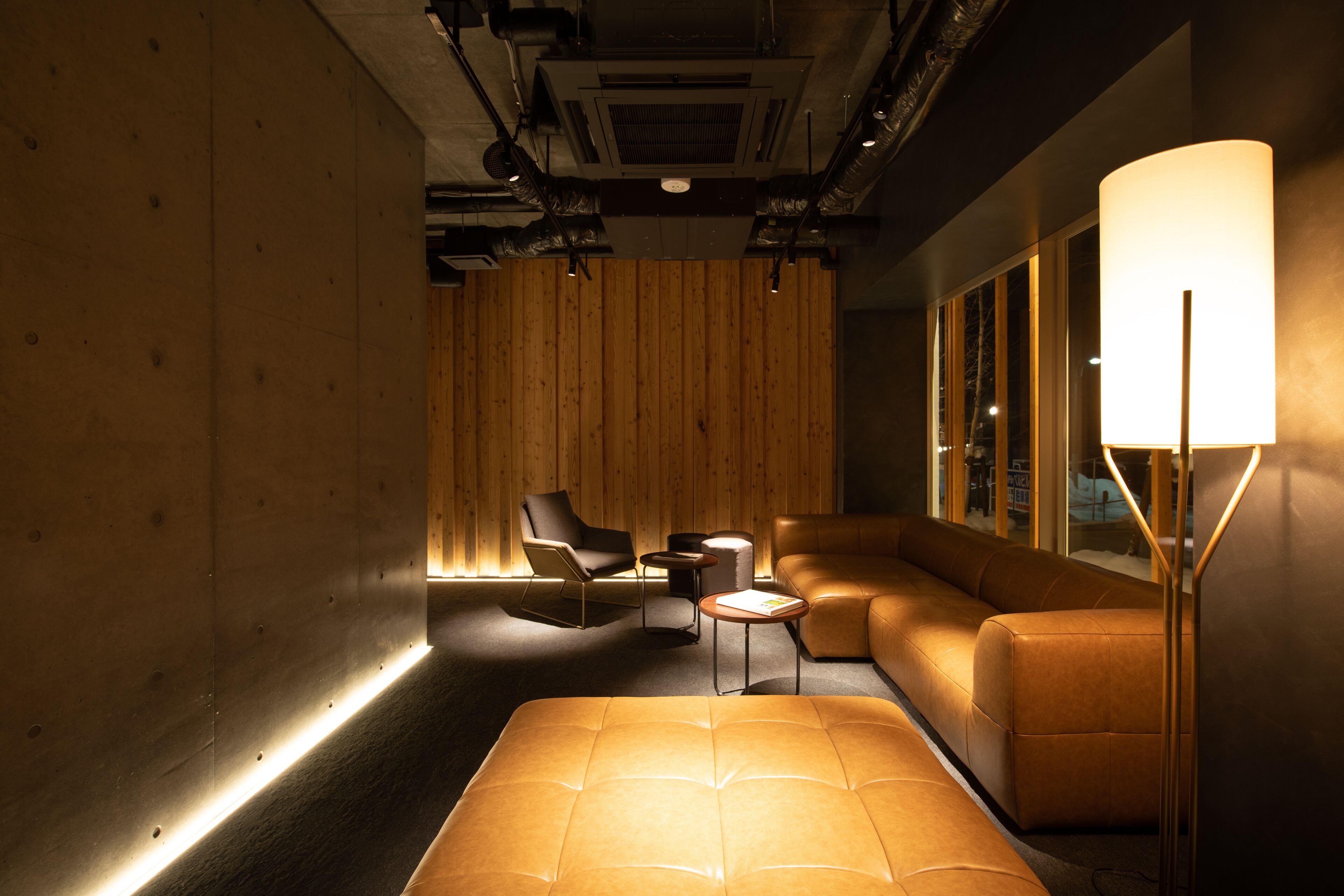 A modern lounge with a wooden wall, leather seating, a floor lamp, and a small table.