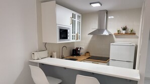 A modern kitchen with white cabinetry, a stainless steel range hood, a built-in oven, a sink, and two white bar stools. - Apartamento Gavines, Miami Playa (Miami Playa)