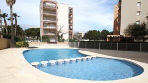 A swimming pool with a curved edge, surrounded by a low fence, and adjacent to a multi-story building with balconies. - Apartamento Gavines, Miami Playa (Miami Playa)