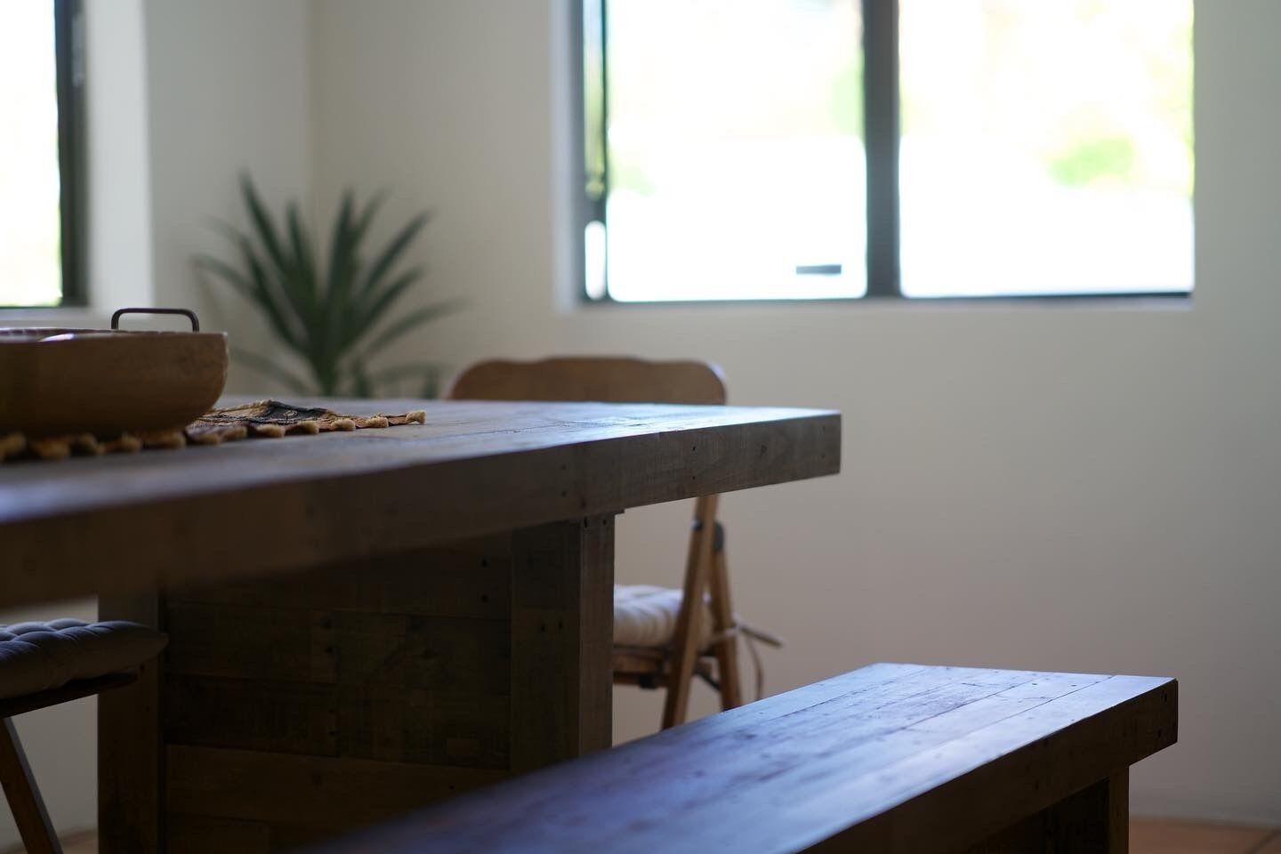 A wooden dining table with a bench, a plant, and a window in the background.