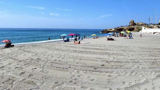 A beach with umbrellas, people, and a rocky outcrop in the background.
