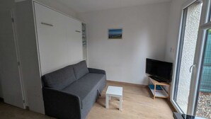 Un espace de vie compact comprenant un canapé, une petite table, un téléviseur posé sur un meuble et une fenêtre donnant sur un paysage agréable.