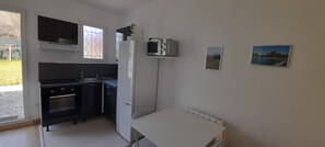 Cocina compacta con refrigerador, microondas, horno y lavabo. Hay dos cuadros en la pared.